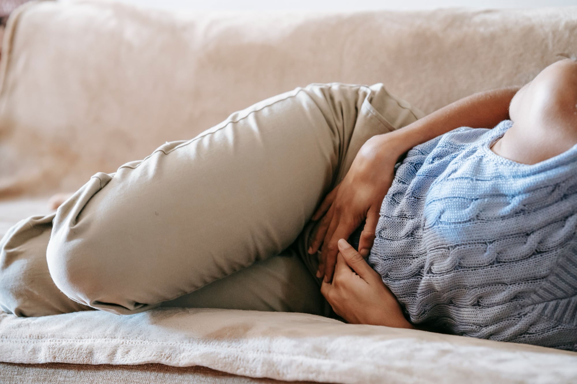 Femme allongée sur un canapé, les mains sur le ventre